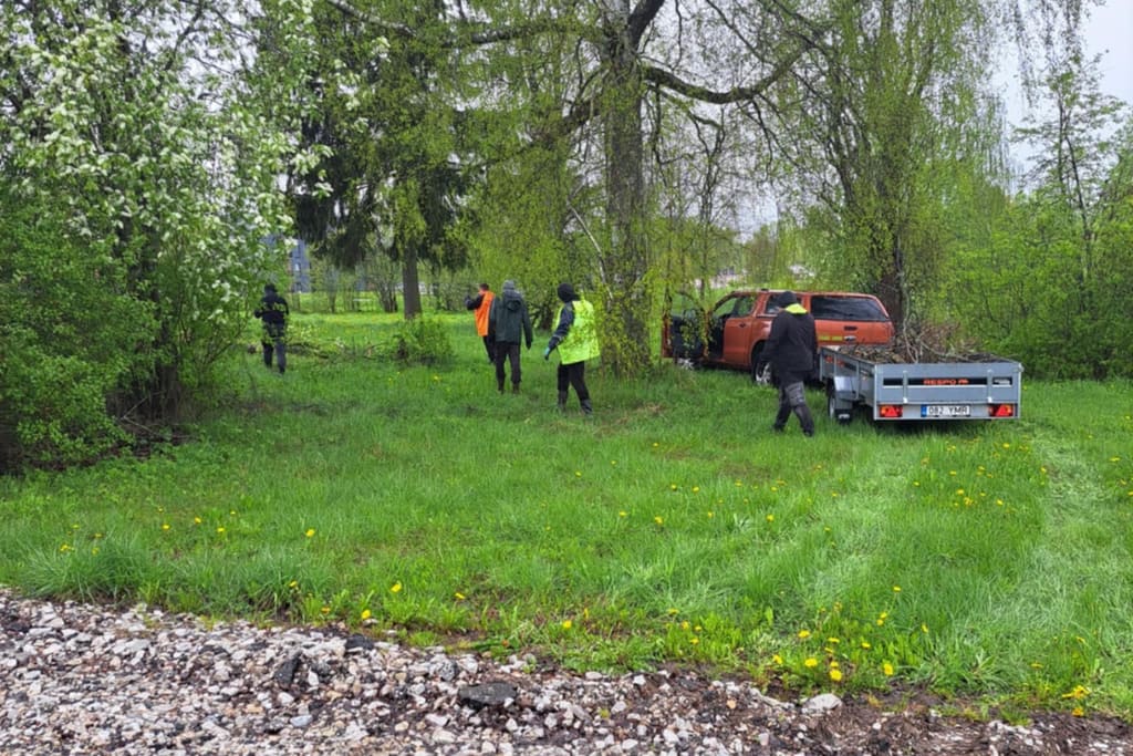 Helkurriietes töömehed raiuvad võsa ja niidavad kõrget rohtu, kõrval pikap koos järelhaagisega
